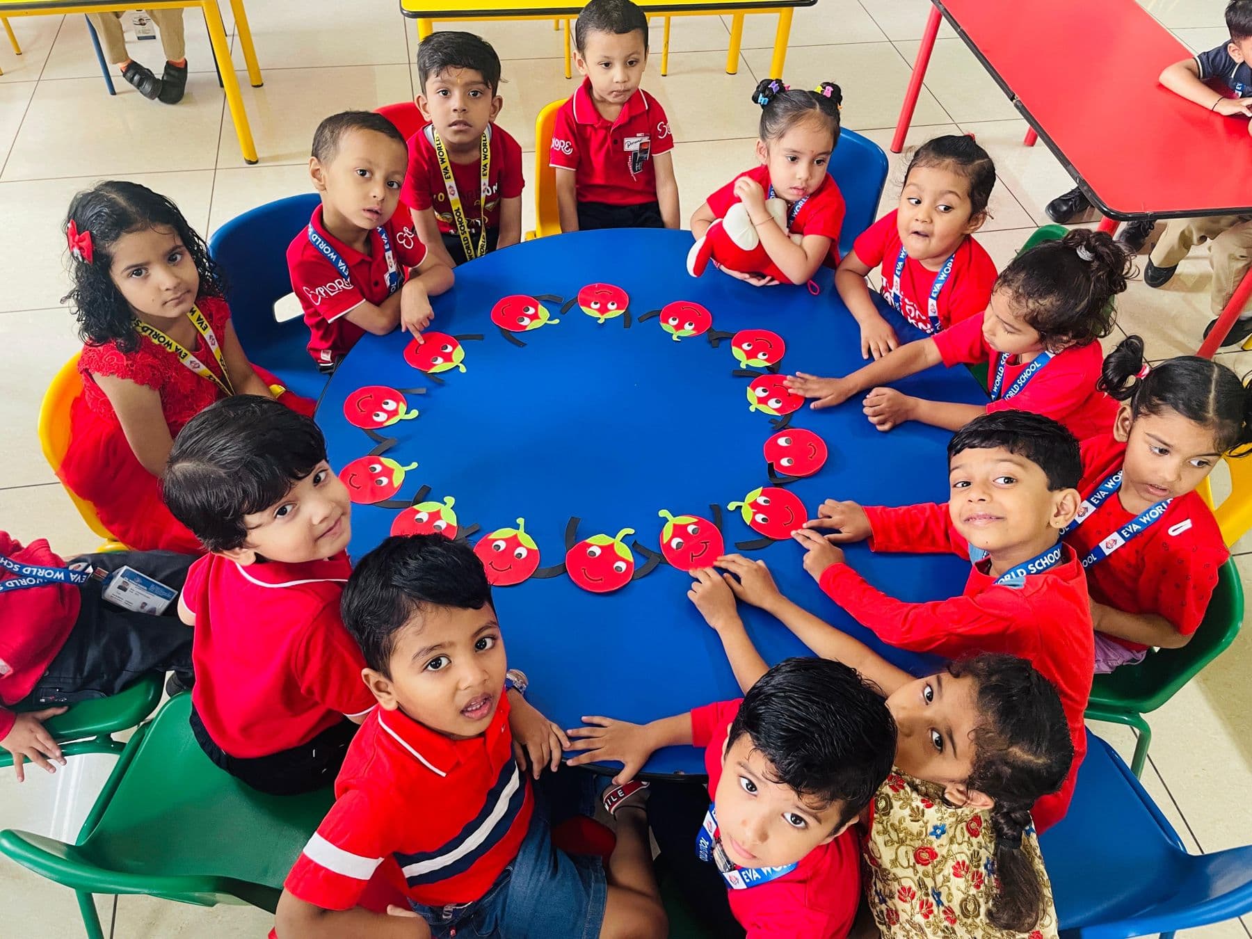 Young children seated in a circle around a blue mat, looking up and smiling