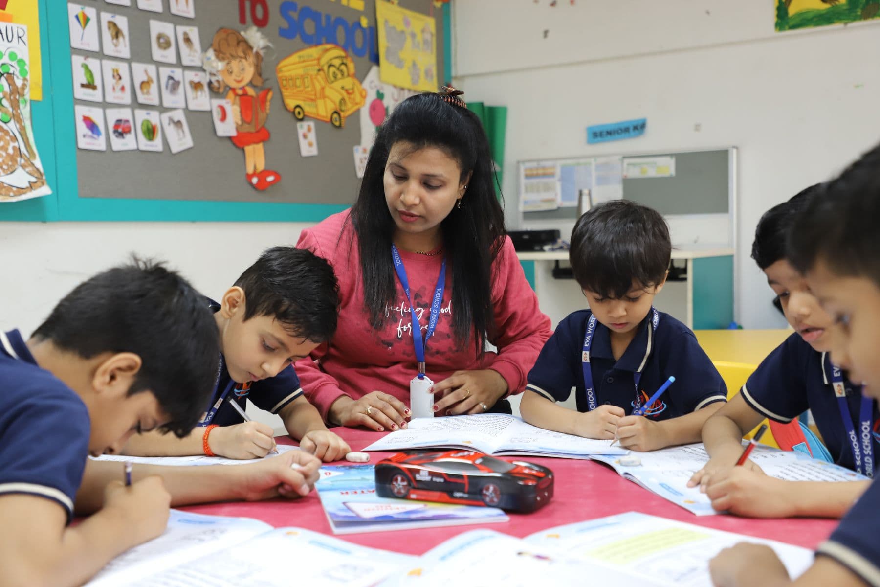 A teacher helping students write at a classroom table